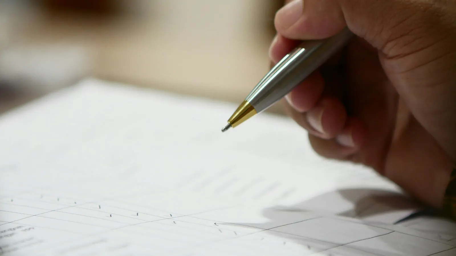 A hand holding a silver and gold pen above a printed form with blank lines