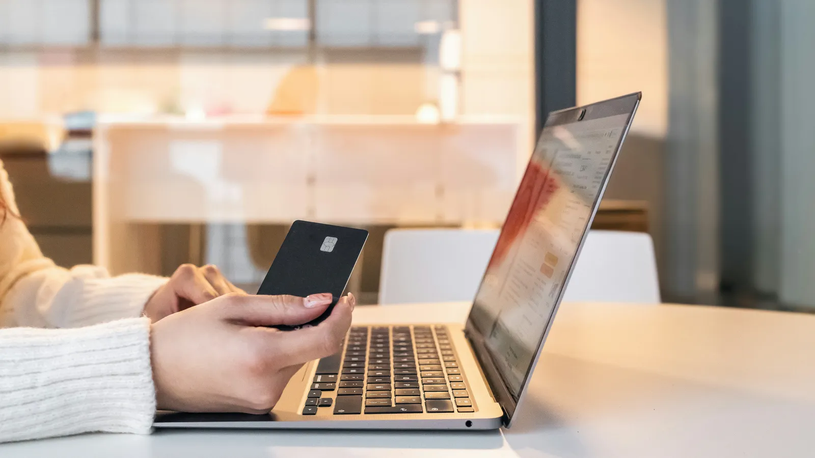 Person holding a payment card while typing on a laptop to pay online