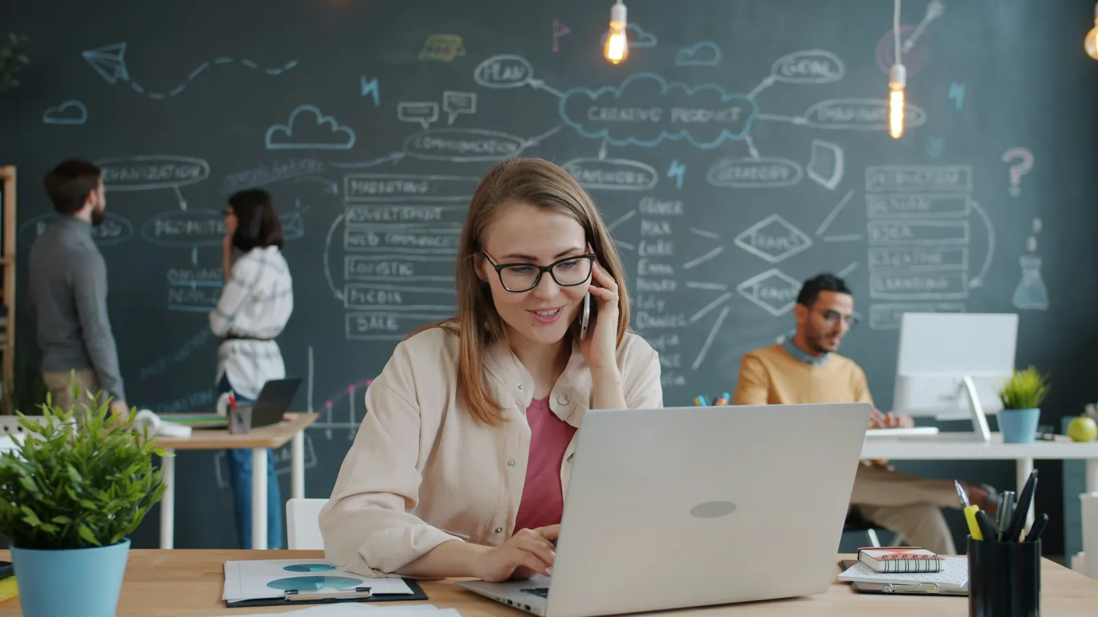 Woman on a phone call typing on a laptop in a shared office