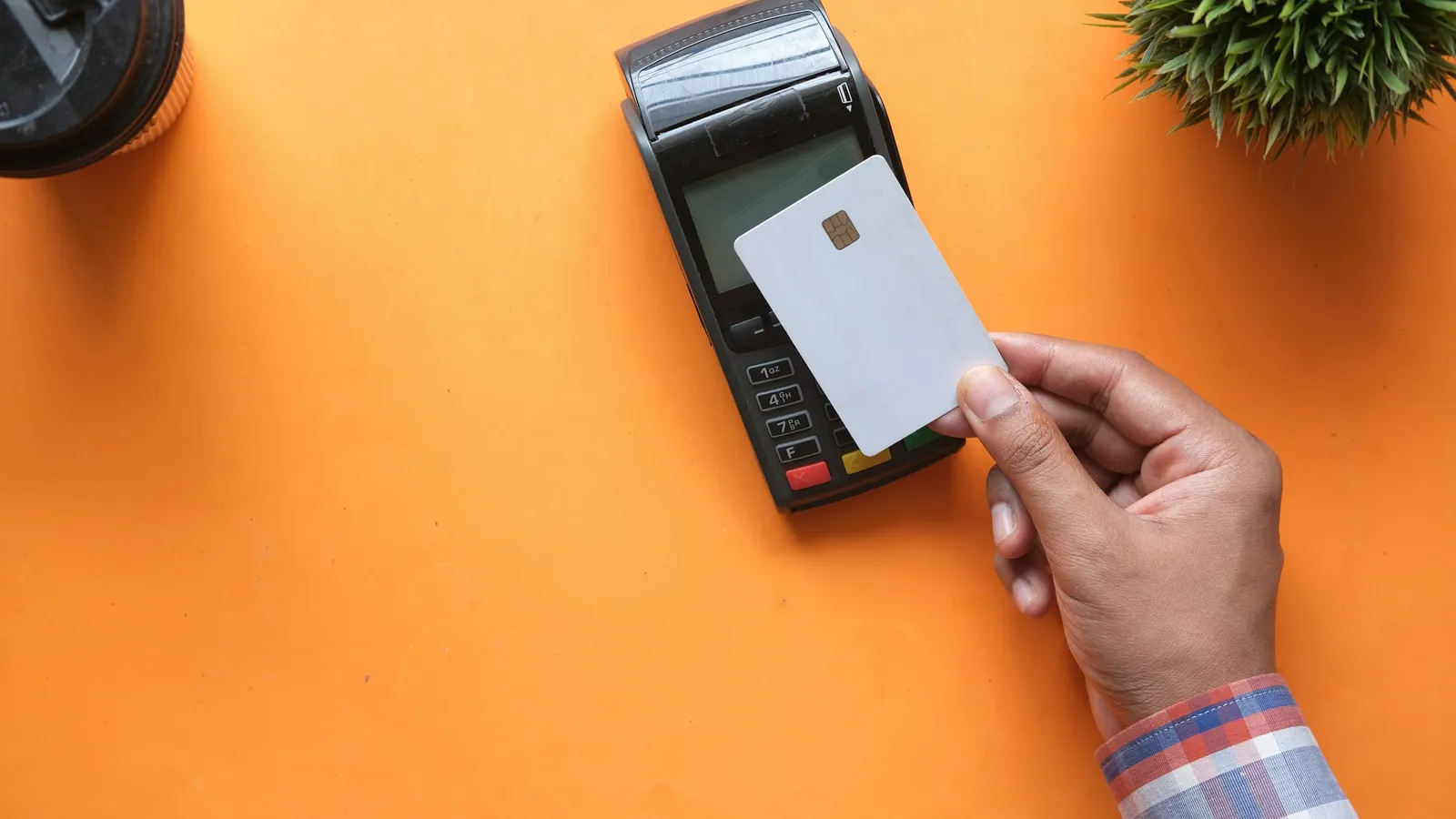 Hand holding a blank card to a card terminal on an orange desk