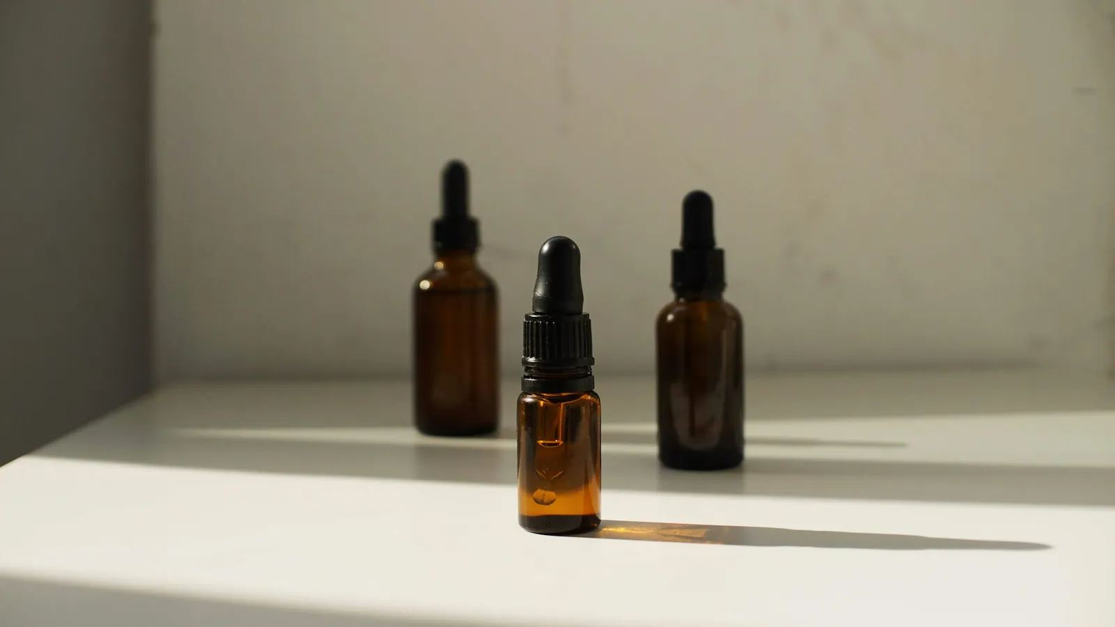 Three unlabeled amber dropper bottles on a white shelf