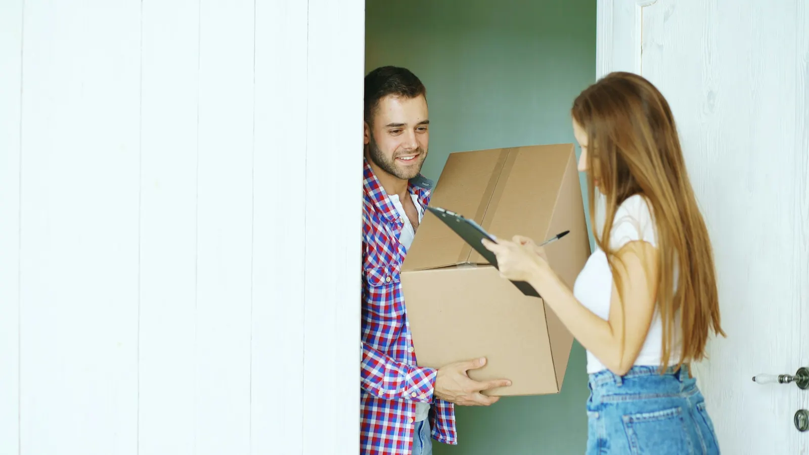 Man delivering a cardboard box to a woman signing a clipboard at her door