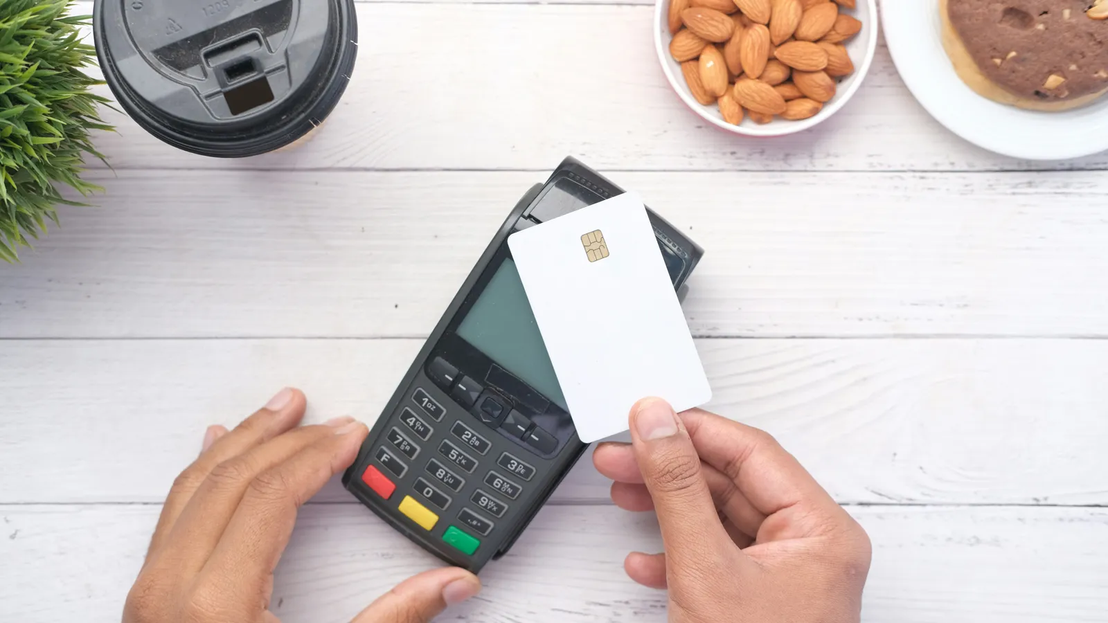Hands holding a blank chip card over a card payment terminal on a white table