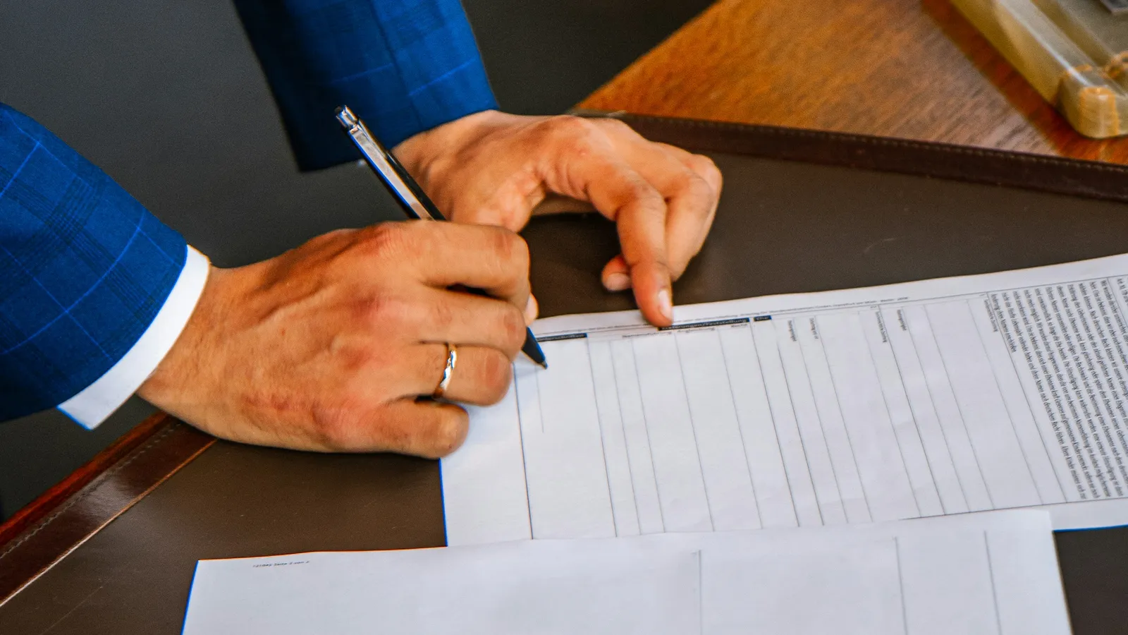 Person in a suit filling out a printed form with a pen