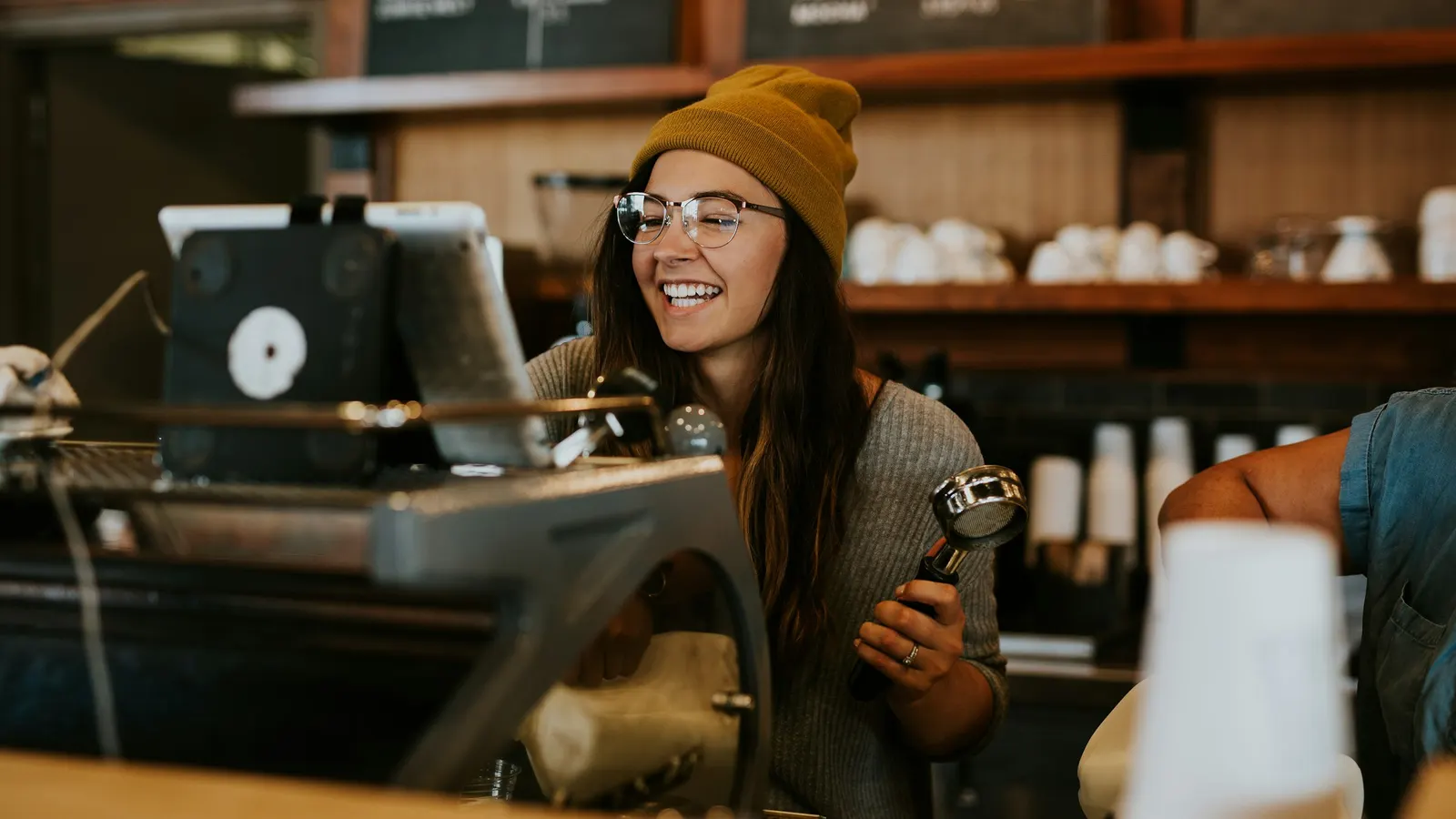 Smiling barista in a knit hat working behind a coffee shop counter