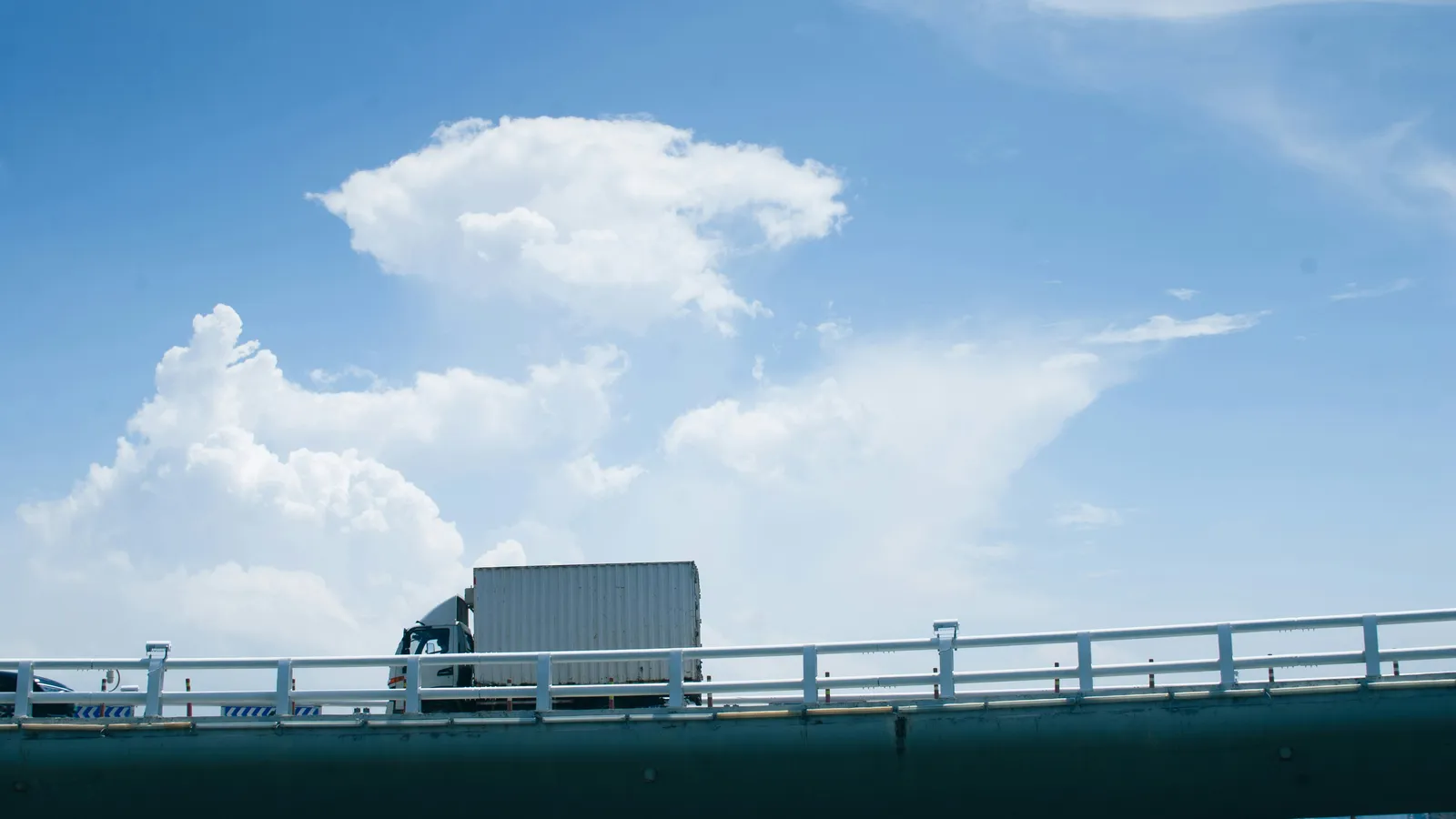White box truck crossing a highway bridge under a blue sky with clouds
