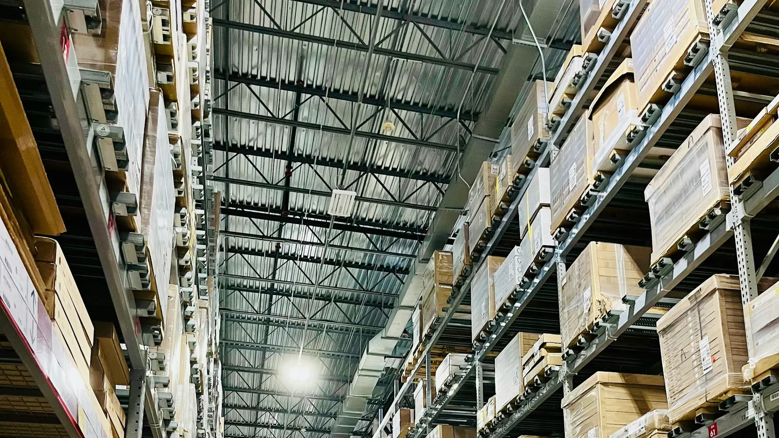 Tall warehouse shelves stacked with cardboard boxes under bright ceiling lights